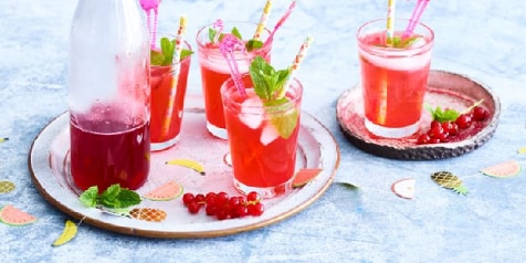 Glazen rode vruchtendrank met ijs en munt, geserveerd op een dienblad met een fles sap.