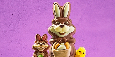 Chocolade paashaas met paaseieren en een geel kuikentje op een paarse achtergrond.