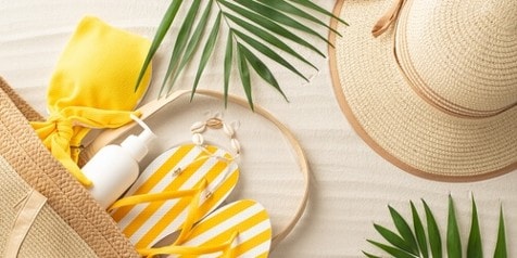 Strandaccessoires met strohoed, zonnebril, gele teenslippers en strandtas.