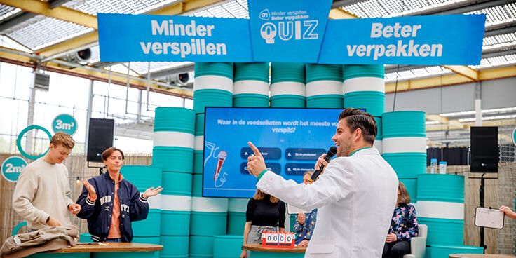 Minder Verspillen Beter Verpakken Quiz evenement met presentator en deelnemers in een interactieve setting.