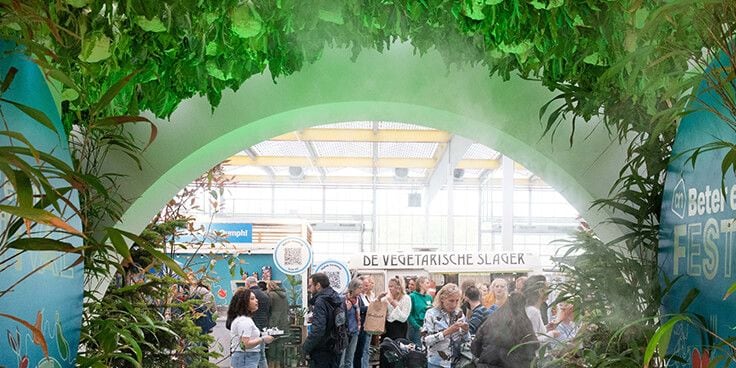 Festivalstand met planten en mist, met op de achtergrond een bord met de tekst "De Vegetarische Slager".