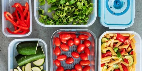 Versnipperde paprika, veldsla, courgette, cherrytomaten en een pastasalade in verschillende opbergdozen