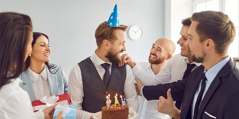 Collega's vieren een verjaardag op kantoor met cadeaus en een chocoladetaart met kaarsjes
