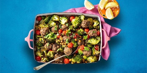 Ovenschotel met gehaktballetjes, broccoli, kikkererwten, tomaatjes en kruiden, geserveerd met partjes citroen.