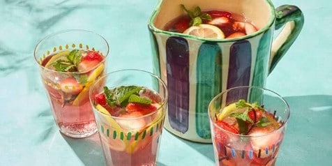 Drankkan met gekoelde fruitpunch, gegarneerd met schijfjes citroen, aardbei en verse munt, geserveerd in glazen.