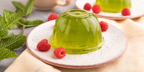 Groene jelly dessert met frambozen op een bord.