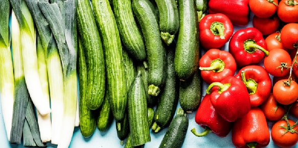 Prei, komkommers, rode paprika's en tomaten naast elkaar op een oppervlak.