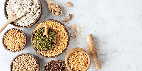 Verschillende soorten peulvruchten en zaden in houten kommen op een marmeren ondergrond.