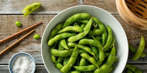Kom met edamame bonen en een schaaltje zeezout op een houten tafel met stokjes.