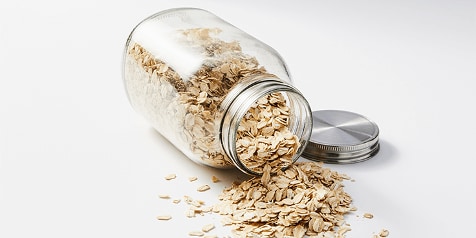 Glazen pot met havermout op witte achtergrond.