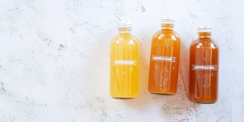 Drie flessen kombucha in verschillende tinten op een lichte achtergrond.