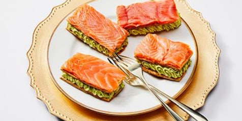 Zalm hapjes op noodles geserveerd op een elegant bord met gouden rand.