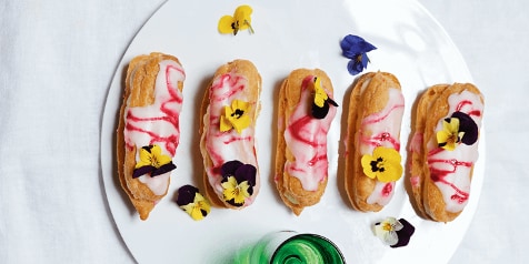 Eclairs met roze glazuur en eetbare bloemen op een witte schaal.