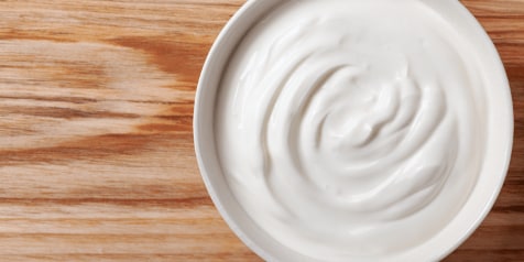 Een kom met romige yoghurt op een houten tafel.