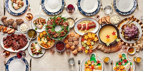 Feestelijke tafel met een uitgebreid kerstdiner, inclusief vleesgerechten, diverse bijgerechten en kleurrijke decoraties.