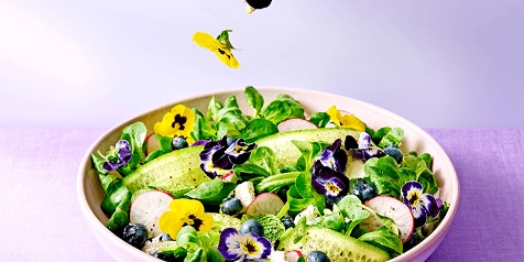 Salade met verse groenten, eetbare bloemen en bosbessen in een kom