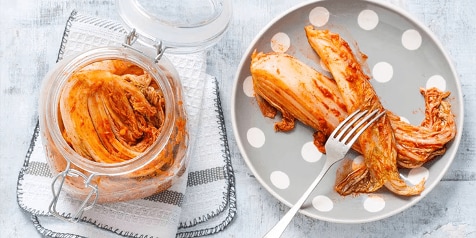 Koreaanse kimchi in een open voorraadpot naast een bord met een portie kimchi.