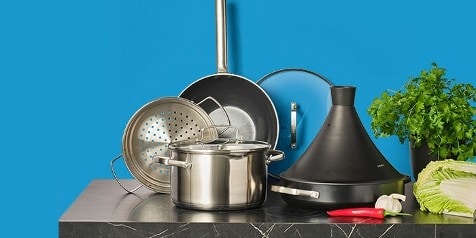 Keukengerei met een stoompan, koekenpan en stoofpot op een marmeren aanrecht, omringd door verse kruiden en groenten.