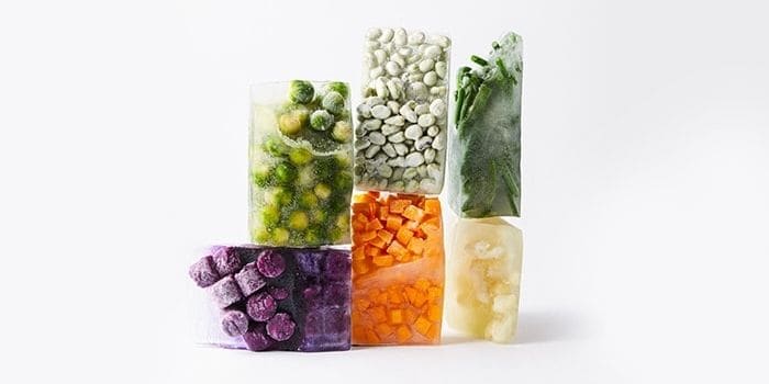 Bevroren groenten en fruit in blokken, waaronder spruitjes, doperwten, bonen, wortelen, aardappelblokjes en paarse bessen.