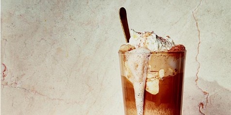 Ijs koffie met slagroom in een glas, geserveerd met een lepel.