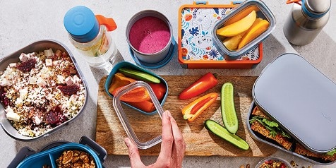 Lunchtrommels met gezonde snacks, waaronder gesneden paprika, komkommer, salade, quinoa met feta en een smoothie.