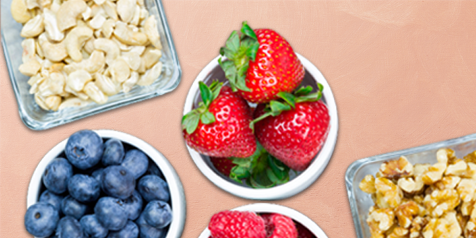 Verschillende schalen met aardbeien, bosbessen, cashewnoten en walnoten.