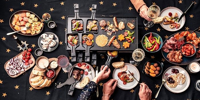 Gezellig gourmetavond met diverse gerechten op een gourmetstel, omringd door borden met bijgerechten, brood en sausjes.
