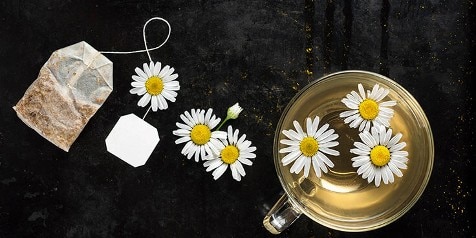 Kamille thee in kopje met kamillebloemen en theezakje op zwarte achtergrond.