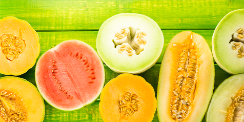 Assortiment van doorgesneden meloenen op een groene achtergrond.