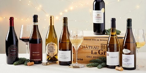 Selectie van verschillende wijnflessen van bekende merken met glazen op een tafel tegen een feestelijk verlichte achtergrond.