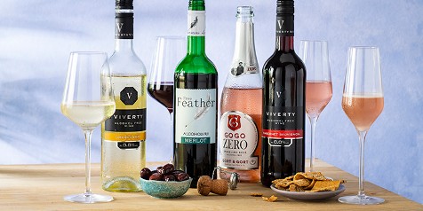 Assortiment van alcoholvrije wijnen met snacks op een tafel, inclusief Viverty Chardonnay, Free Feather Merlot, Gogo Zero Sparkling Rosé en Viverty Cabernet Sauvignon.