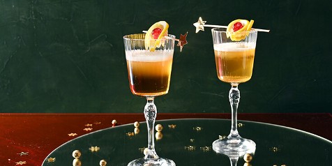 Twee glazen feestelijke cocktails met een garnering van citroen en kers.