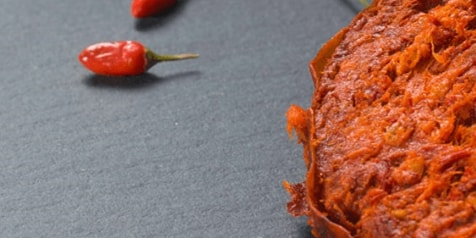 Rood chilipeperpasta met kleine rode chilipepers op een donkere achtergrond