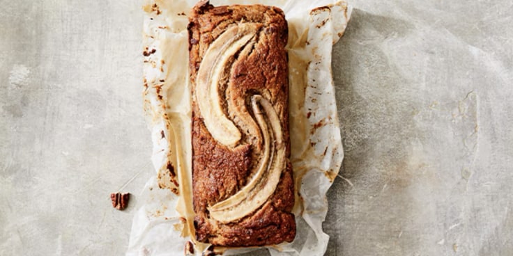 Bananenbrood op bakpapier met pecannoten eromheen.