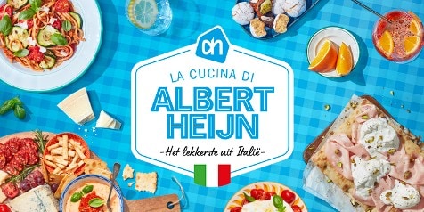 Een blauwe tafellaken met diverse Italiaanse gerechten, waaronder pasta, vleeswaren, kaas, gebak, drankjes en de tekst "La Cucina di Albert Heijn - Het lekkerste uit Italië" met een Italiaanse vlag en Albert Heijn logo centraal.