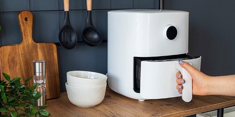 Witte airfryer op een keukenplank met een hand die de lade opent.