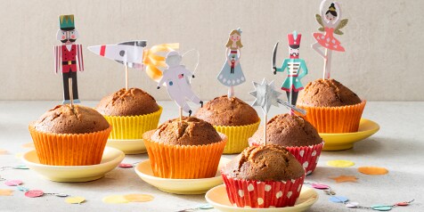 Muffins in kleurrijke papieren vormpjes op schoteltjes, versierd met feestelijke prikkertjes met sprookjesfiguren en confetti op de tafel