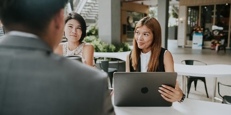 Drie mensen zitten aan een tafel in een moderne kantooromgeving, met een laptop open op tafel.