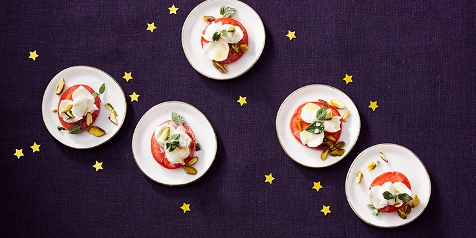 Caprese salade met tomaat, mozzarella en basilicum op witte borden op een donkerblauwe tafel.