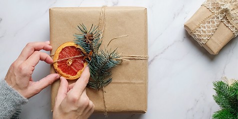 Cadeau verpakt met bruin papier, versierd met schijf gedroogde sinaasappel, dennennaalden en anijsster.