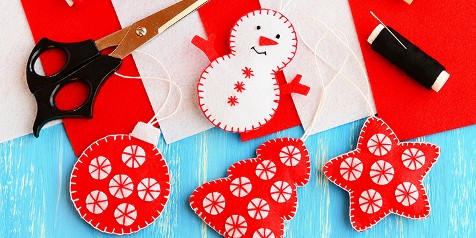 Zelfgemaakte kerstversieringen van vilt met sneeuwpop, bal en ster vormen, met schaar en zwarte draad.