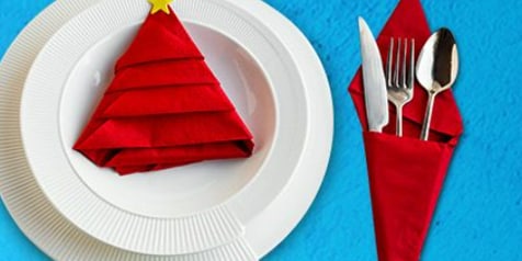 Serviesset met witte borden en rood servet gevouwen in de vorm van een kerstboom, inclusief bestek.