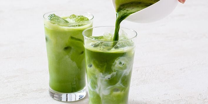 Twee glazen groene ijsthee met melk, waarvan één wordt ingeschonken.