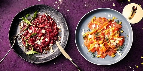 Twee feestelijke gerechten op borden: links rode bietensalade en rechts zalmcarpaccio met dille en kaasschilfers.