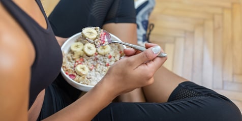 Persoon in sportkleding eet havermout met banaan en bessen uit een kom