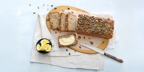 Volkorenbrood met zaden, gesneden op een houten plank, met een mes en een schaaltje boter erbij.