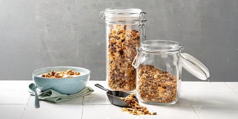 Zelfgemaakte granola in glazen potten naast een kom met yoghurt en granola.
