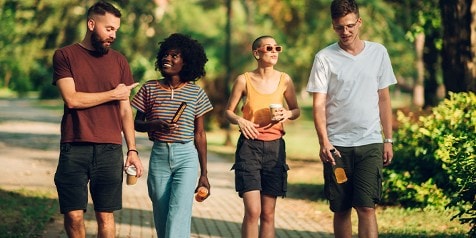 Vier jonge mensen wandelen samen in een park en dragen drankjes in hun handen