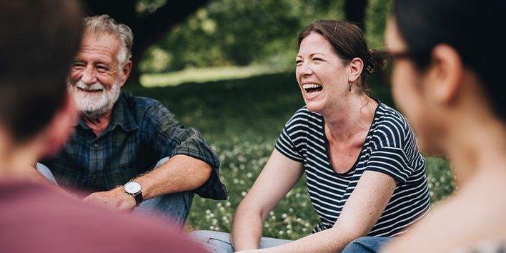 Groep mensen die buiten samen in het gras zitten en met elkaar in gesprek zijn