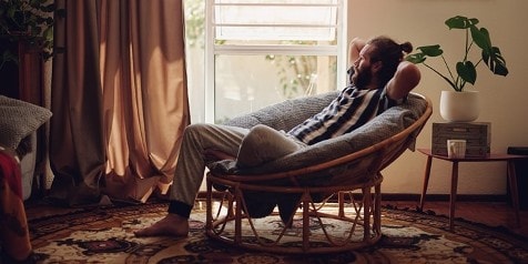 Persoon ontspannen in een rotanstoel bij een raam in een woonkamer.